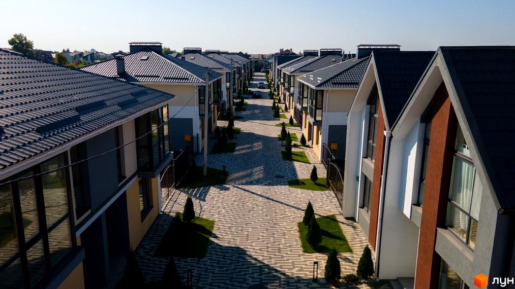 Котеджне містечко КМ Beverly Hills Residence з сучасними фасадами та акуратними зеленими зонами. Фотографія демонструє вулицю з двоповерховими будинками та бруківкою.