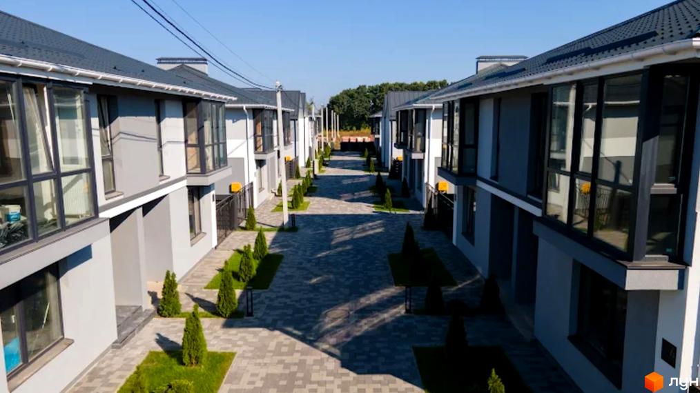 Ряд двоповерхових будинків з великими вікнами та сірими дахами. Перед будинками доглянута територія з бруківкою та зеленими насадженнями.