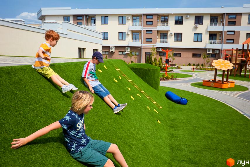 Житловий комплекс GREEN LAND: діти граються на зеленому пагорбі біля багатоповерхових будинків. На території є дитячі майданчики та пісочниця.