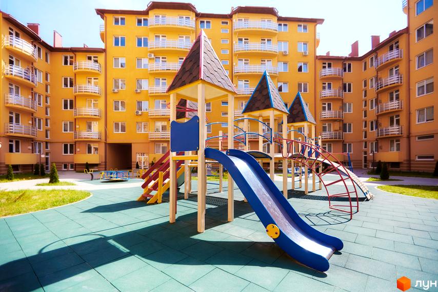 Житловий комплекс САКУРА: жовті багатоповерхові будинки з балконами та дитячий майданчик з гірками та гойдалками.
