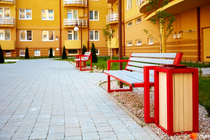 Житловий комплекс САКУРА: жовті фасади будівель, білі вікна та балкони. Прибудинкова територія з бруківкою, зеленими насадженнями та місцями для відпочинку.