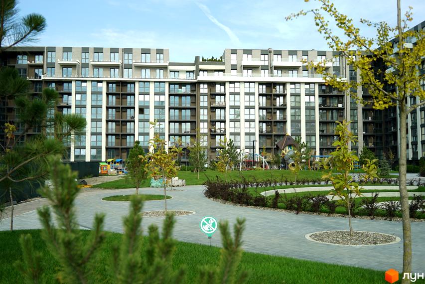 Новобудова ЖК PARK LAND з фасадами з сірої та білої плитки, численними балконами та панорамними вікнами. Прибудинкова територія з зеленими газонами, деревами та дитячим майданчиком.