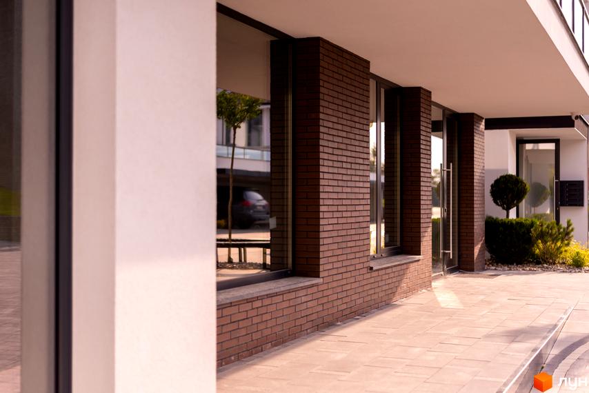 Зовнішній вигляд новобудови ЖК SHERWOOD з цегляним фасадом та великими вікнами. Прибудинкова територія з бруківкою та зеленими насадженнями.