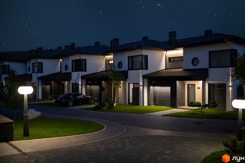 Котеджне містечко КМ SHERWOOD. Сучасні двоповерхові будинки з гаражами та доглянутою прибудинковою територією під зоряним небом. На території є освітлення та зелені насадження.