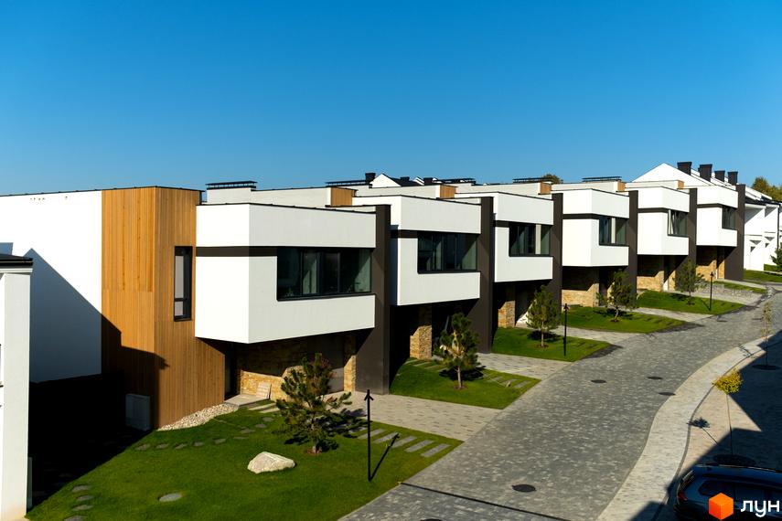 Котеджне містечко SHERWOOD з білими фасадами, дерев'яними елементами та темними акцентами. Охайний двір з газоном, бруківкою та молодими деревами.