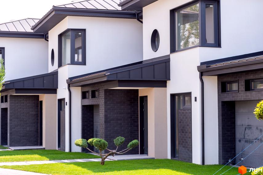 Котеджне містечко SHERWOOD: фасади будинків з білою штукатуркою та темною цеглою, темні дахи. Зелена галявина та доріжка перед будинками.