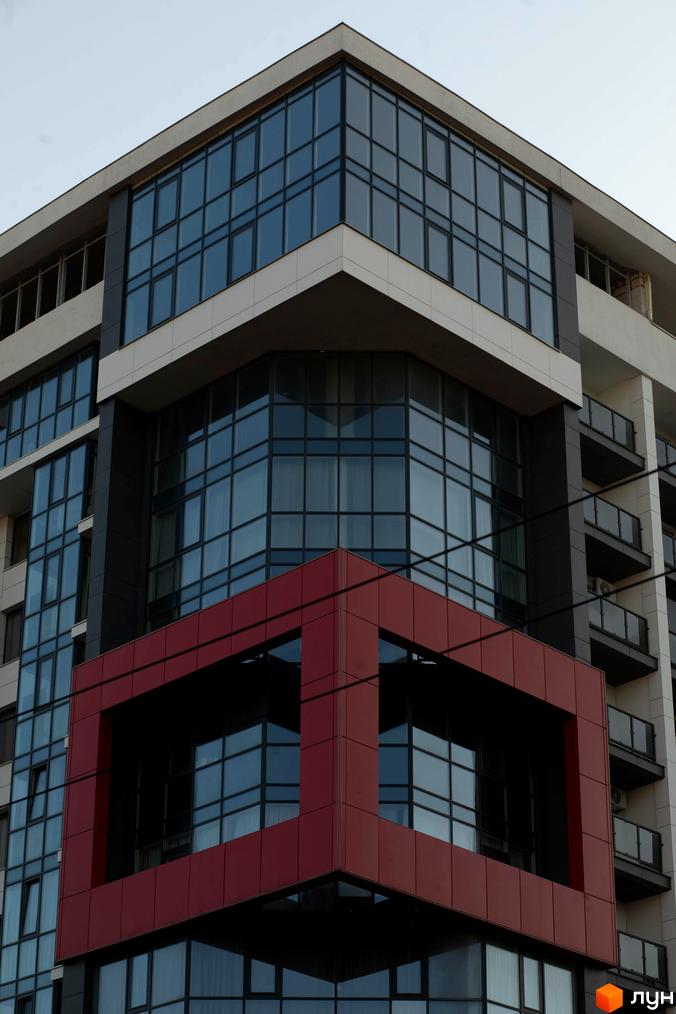 Зображення фасаду Новобудови Cube House з великими вікнами та червоним кубічним елементом. Архітектура будинку та скління.