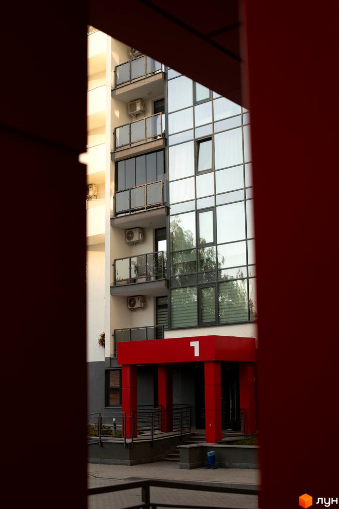 Фасад Житлового комплексу Cube House з великими скляними вікнами та балконами. Червоний вхід з номером 1 та доріжка до будівлі.