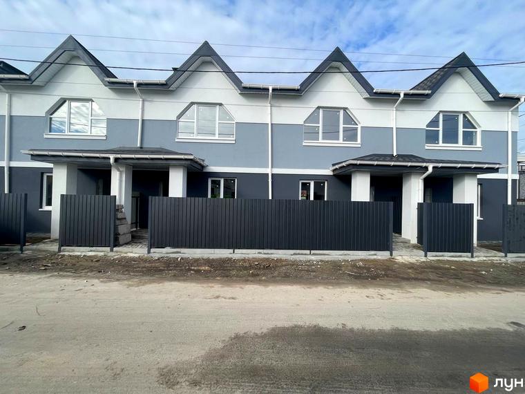 Зображення таунхаусів житлового комплексу «Комфортне містечко» з темним парканом та асфальтованою дорогою перед ними. Будинки мають двоколірний фасад та трикутний дах.