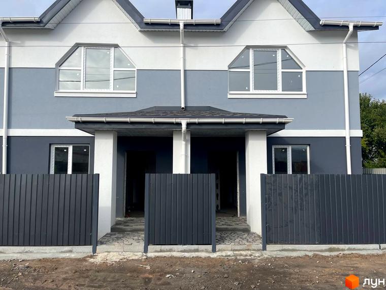 Таунхаус „Комфортне містечко“ з сіро-білим фасадом та великими вікнами. Перед будинком темно-сірий паркан і доріжка з бруківки.