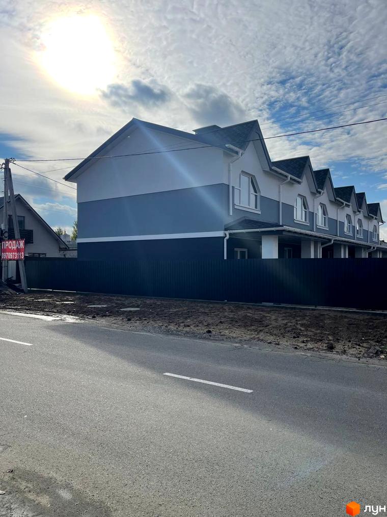 Зображення сторінки житлового комплексу Таунхауси „Комфортне містечко“. На фото ряд двоповерхових будинків з трикутними дахами, огороджені парканом, перед будинками асфальтована дорога.