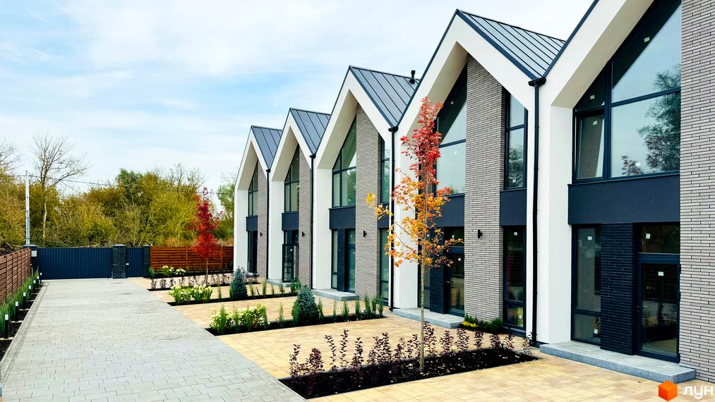 Таунхауси FreeDOM's з сірою цегляною кладкою та великими вікнами, розташовані на бруківці з зеленими насадженнями.