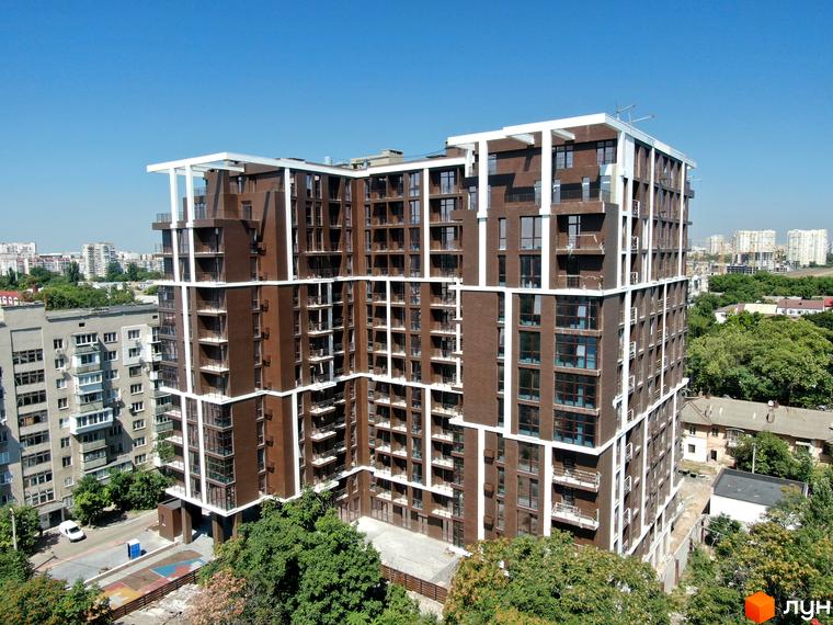 Висотна новобудова ЖК Пространство на Гераневій з коричневою цегляною кладкою та білими лініями на фасаді, навколо зелені дерева та блакитне небо.