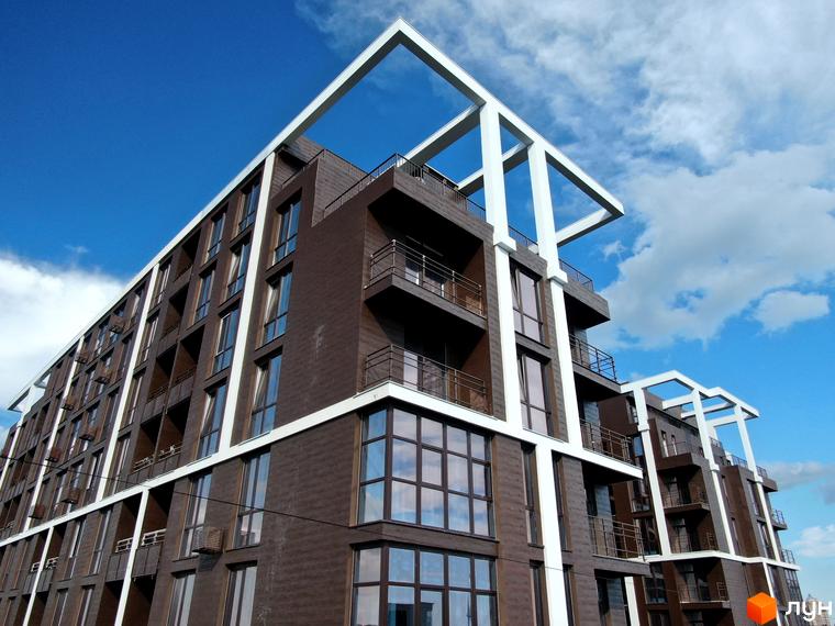 Висотна будівля ЖК Пространство на Гераневій з великими вікнами та балконами, білі архітектурні елементи на фасаді, блакитне небо з хмарами.