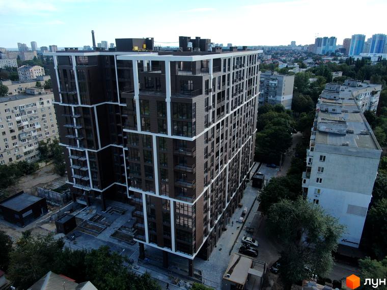 Висотна новобудова Пространство на Гераневій з панорамними вікнами та білими обрамленнями. На прибудинковій території видно парковку та зелені насадження.