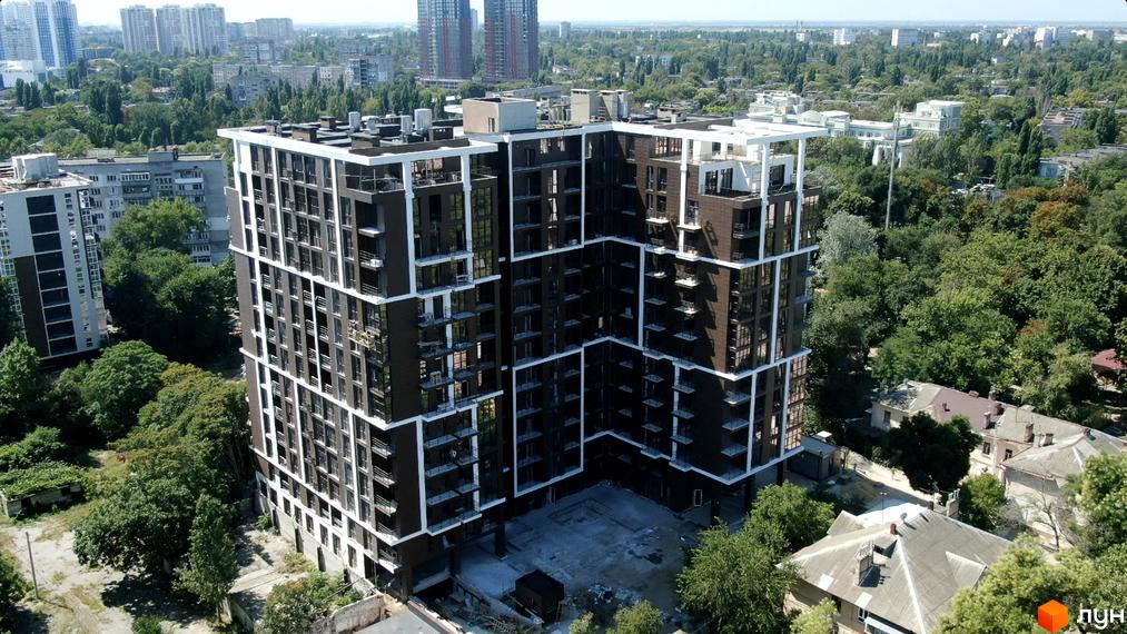 Висотна новобудова ЖК Пространство на Гераневій з темними фасадами та білими обрамленнями вікон, навколо зелені дерева та будинки старої забудови.