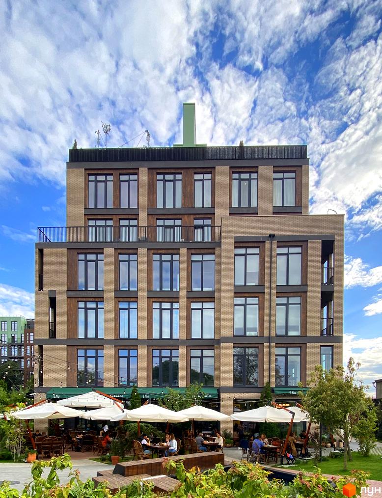 Зображення фасаду Житлового комплексу Пространство на Донського з великими вікнами та літнім майданчиком ресторану внизу.