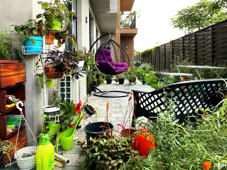 Зовнішній вигляд будинку та прибудинкової території Житлового комплексу Пространство на Донського. На подвір'ї багато рослин та підвісне крісло.