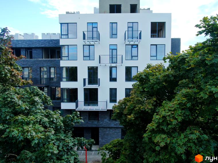 Простір на 9-й Фонтана – це житловий комплекс з білими та темними фасадами, балконами та великими вікнами, оточений зеленню дерев.