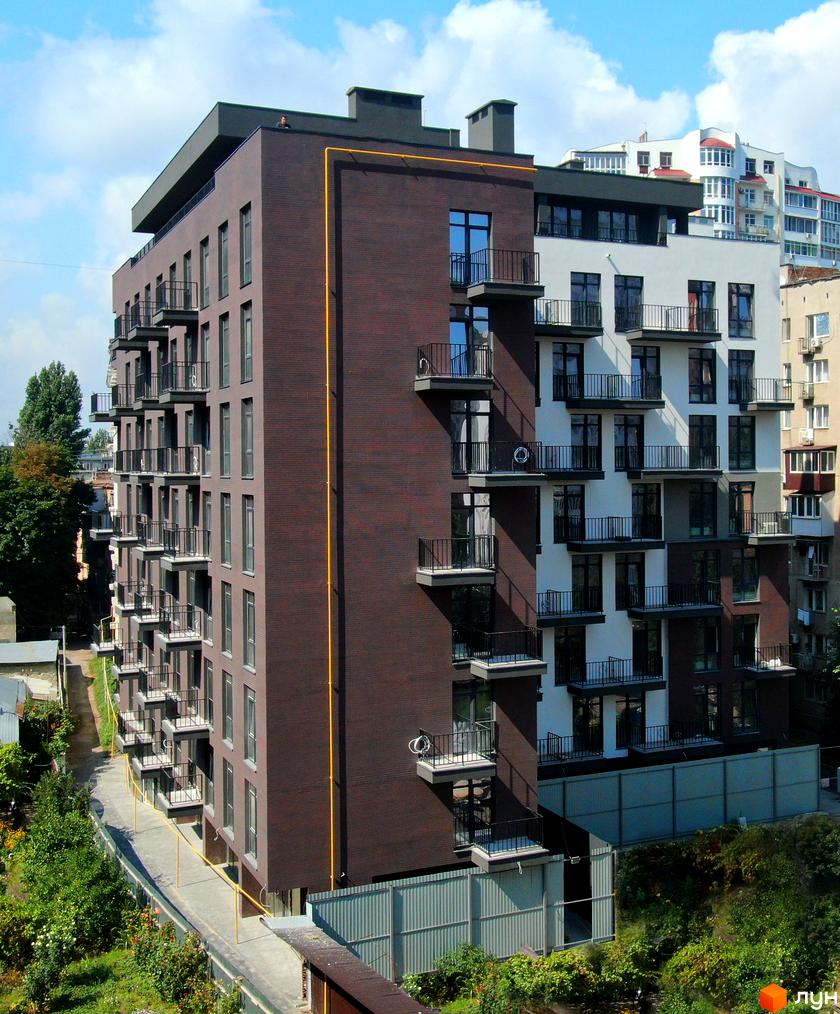 Зовнішній вигляд житлового комплексу Пространство на Педагогической з коричневої цегли та білої штукатурки, з балконами та вікнами. Навколо будинку зелені насадження та доріжка.