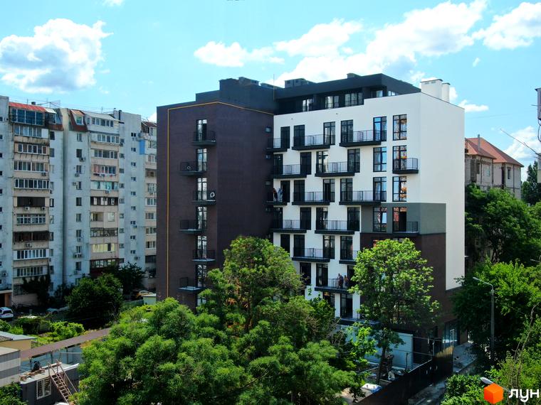 Новобудова Пространство на Педагогической з білими та коричневими фасадами, балконами та вікнами на тлі блакитного неба з хмарами. Навколо зелені дерева та сусідні будівлі.