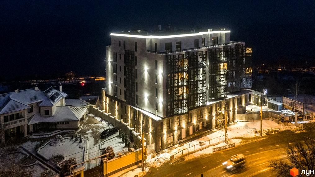 Простір на 12-й Фонтана - це новобудова з виразним фасадом, підсвіченим вночі, та прилеглою територією зі снігом та будинком.