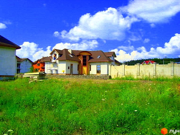 Будинок житлового комплексу КМ Лісове озеро з червоною покрівлею на фоні зеленого газону та блакитного неба.