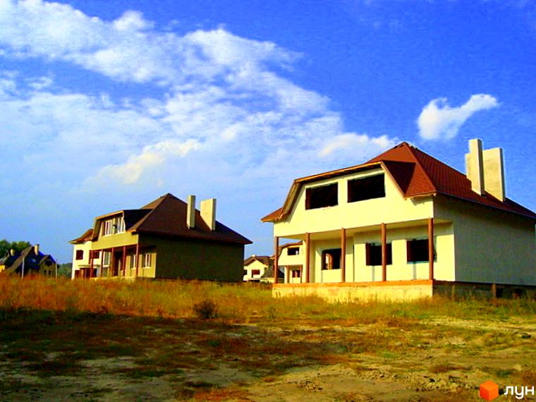 Будинки житлового комплексу КМ Лісове озеро з червоними дахами на фоні блакитного неба. Прибудинкова територія з зеленими насадженнями та відкритим простором.