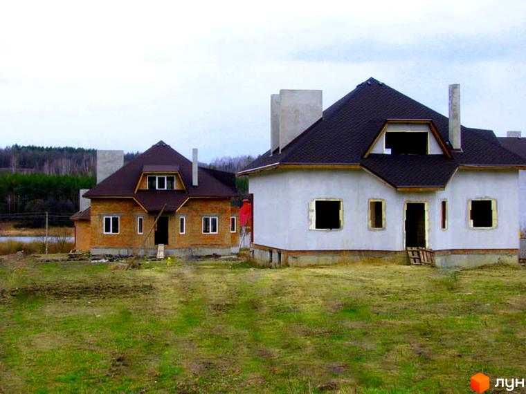 Котеджне містечко Лісове озеро: двоповерхові будинки з темними дахами на етапі будівництва. Навколо будинків зелена трава та дерева.