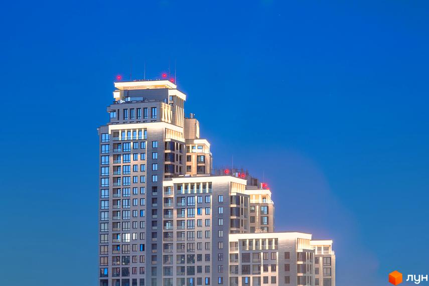 Житловий комплекс Crystal Park Tower - висотна новобудова з панорамними вікнами та червоними сигнальними вогнями на даху на фоні блакитного неба.