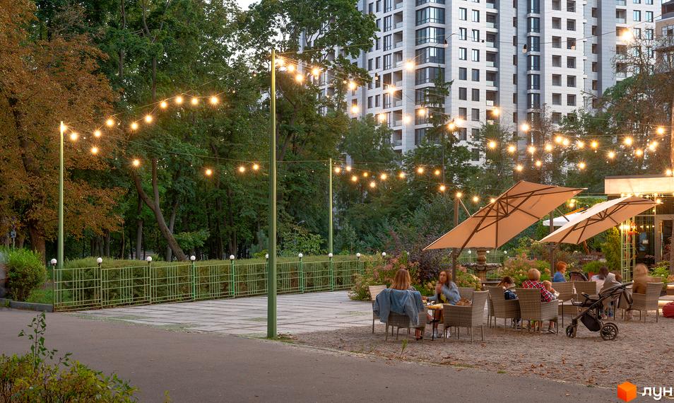 Житловий комплекс Crystal Park Tower з освітленням та місцями для відпочинку на прибудинковій території. Сучасна архітектура будівлі та зелена зона.