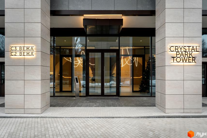 Житловий комплекс Crystal Park Tower з підсвіченими вивісками та вхідною групою. Прибудинкова територія вимощена плиткою.