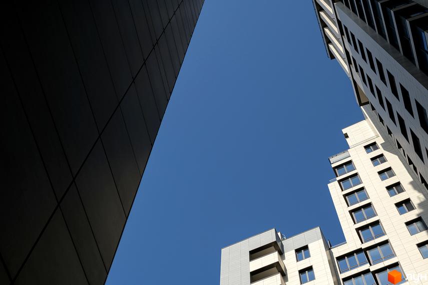 Житловий комплекс Crystal Park Tower з фасадами з темних панелей та світлої плитки. Вид знизу на будівлі та синє небо.