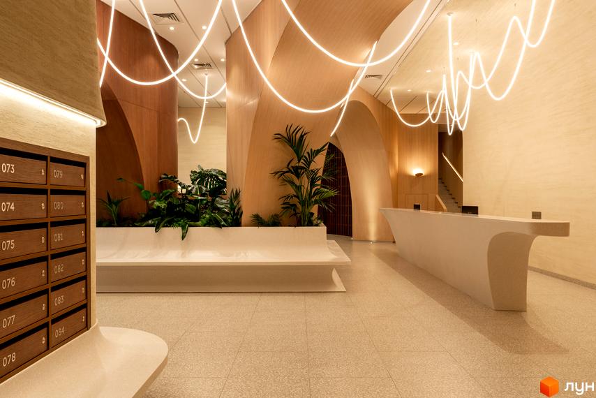 Лобі житлового комплексу Crystal Park Tower з дизайнерським освітленням та зоною відпочинку з рослинами. Оздоблення натуральними матеріалами створює затишну атмосферу.