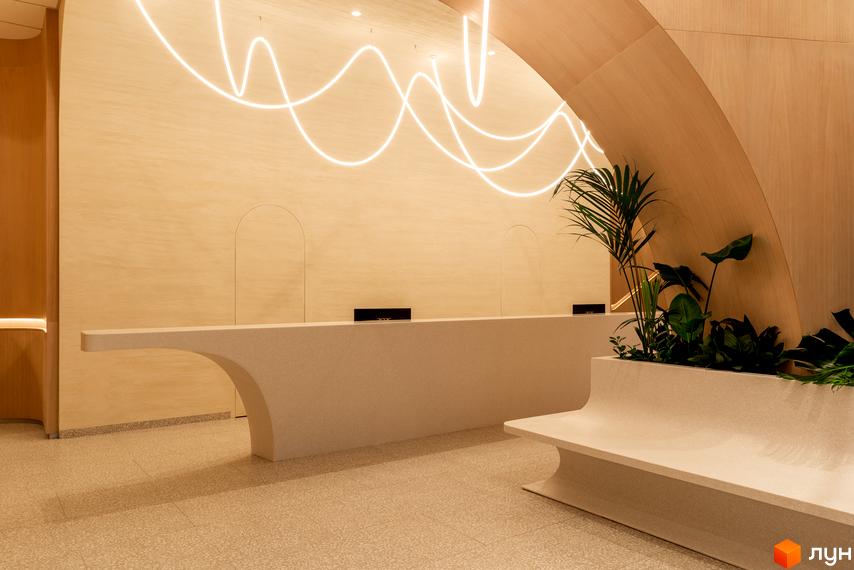 Інтер'єр рецепції житлового комплексу Crystal Park Tower з вигнутою стійкою та неоновим освітленням. Зелені рослини додають затишку.