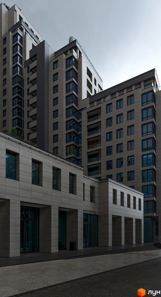 Зовнішній вигляд житлового комплексу Crystal Park Tower з кам'яним фасадом та великими вікнами. Перед будівлею розташований вимощений бруківкою двір.