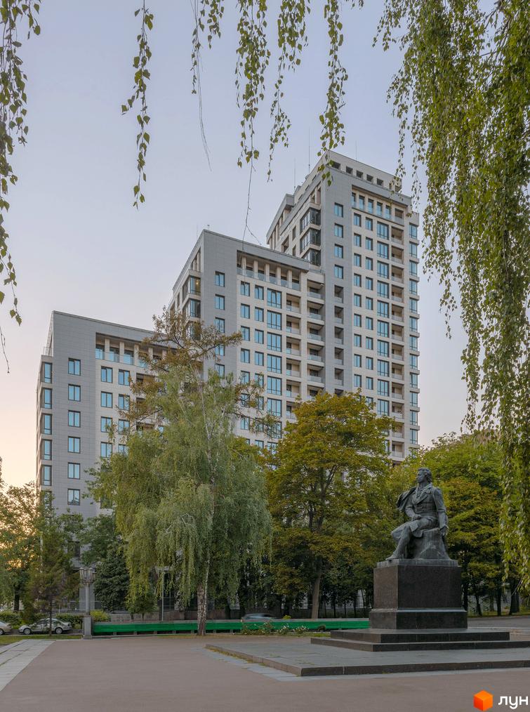 Житловий комплекс Crystal Park Tower з сірими фасадами та численними вікнами, розташований біля парку з пам'ятником та деревами.