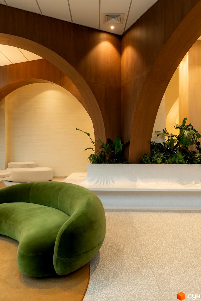 Інтер'єр ЖК Crystal Park Tower з зеленим диваном та рослинами у білій кашпо під арками з дерева.