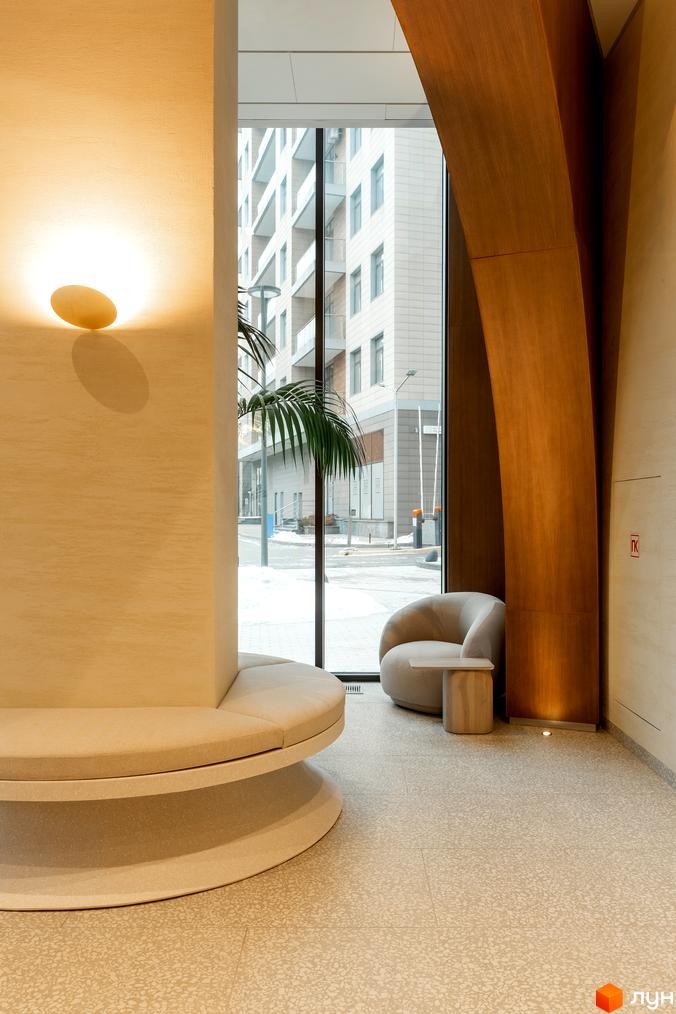 Інтер'єр ЖК Crystal Park Tower з круглим диваном і кріслом біля великого вікна з видом на будівлі.