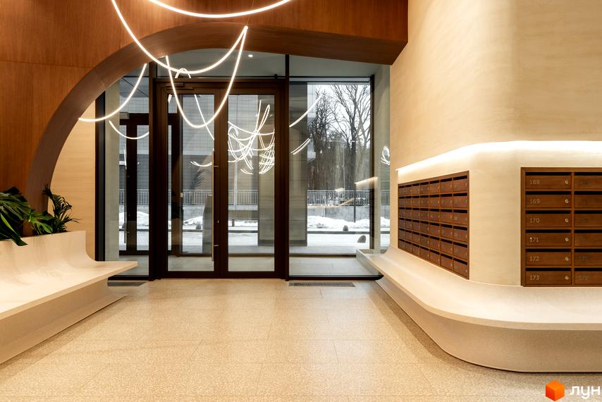 Сучасний вхід у ЖК Crystal Park Tower з дизайнерськими світильниками та зручними лавками. Просторий хол з поштовими скриньками та великими вікнами, що виходять на прибудинкову територію.
