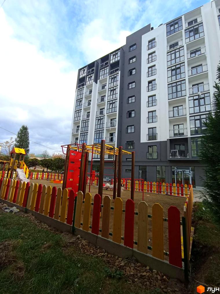 Житловий комплекс Сонячна Долина з фасадом з білих та сірих панелей, дитячий майданчик з кольоровою огорожею на прибудинковій території.