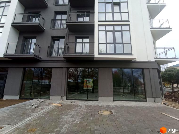 Фасад житлового комплексу ЖК Сонячна Долина з великими вікнами та балконами. Поруч облаштована прибудинкова територія з бруківкою.
