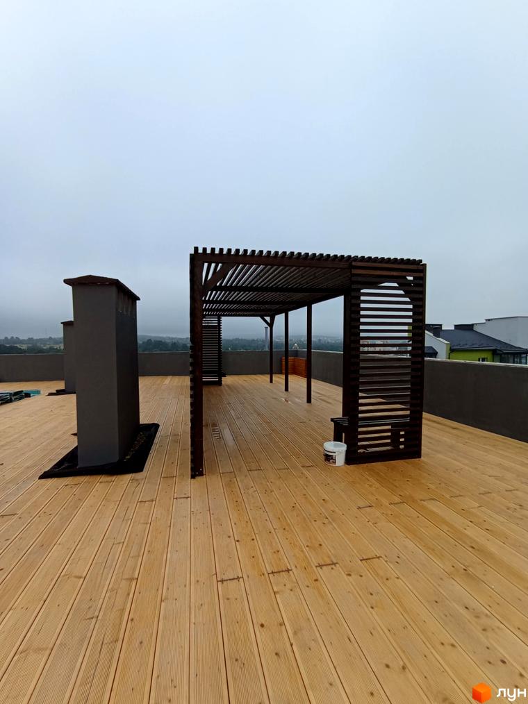 Тераса на даху Житлового комплексу Сонячна Долина з дерев'яним настилом, перголою та димоходом. Відкритий простір для відпочинку.