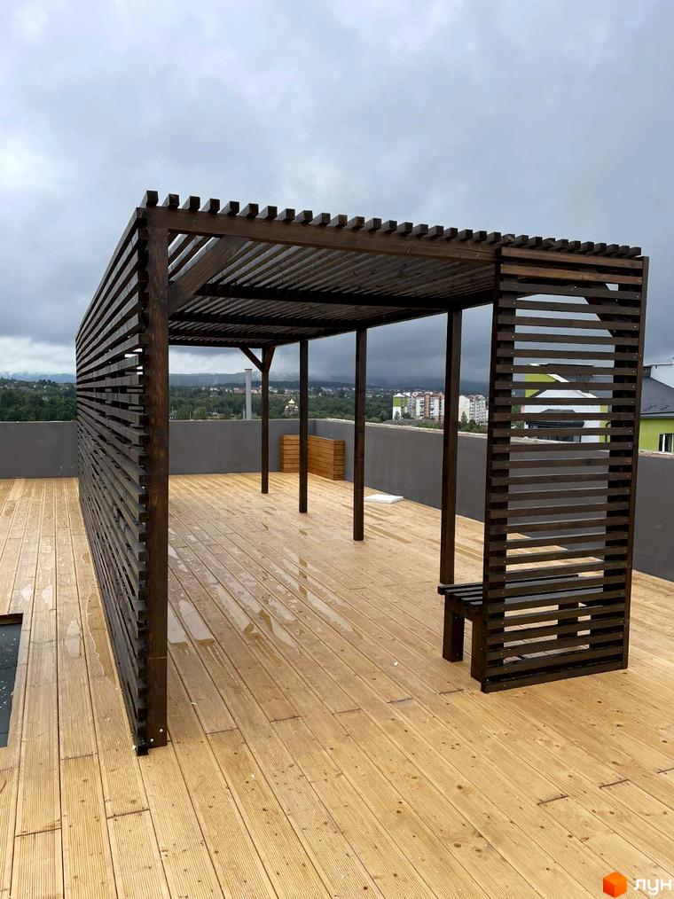 Житловий комплекс Сонячна Долина: дерев'яна альтанка з лавкою на терасі з дерев'яним настилом, що виходить на міський пейзаж.