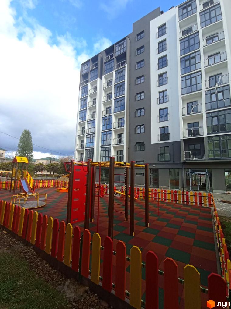 Зовнішній вигляд багатоповерхового будинку ЖК Сонячна Долина з великими вікнами та балконами, поруч дитячий майданчик з яскравим огородженням.