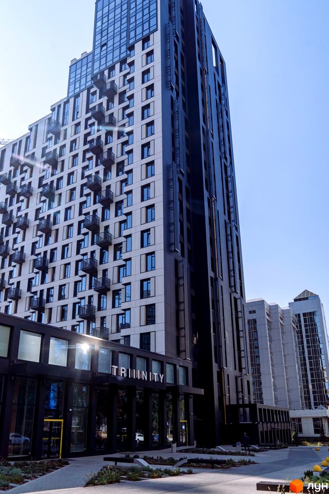 Зовнішній вигляд житлового комплексу TRIIINITY з високою вежею та балконами. Прибудинкова територія з доріжками та зеленими насадженнями.