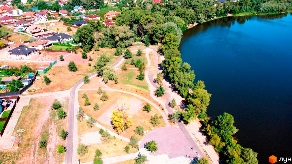 Котеджне містечко КМ Міжріччя з видом на озеро та зелені насадження. На території комплексу розташовані доглянуті алеї та зони відпочинку.