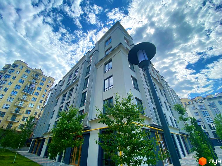 Зображення фасаду та прибудинкової території Житлового комплексу Бургундія. Багатоповерховий будинок з великими вікнами та зеленими насадженнями.