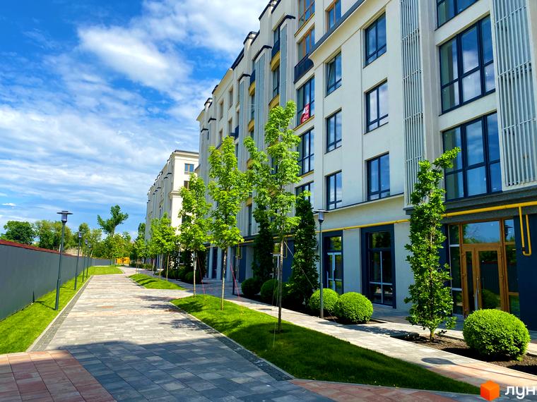 Зовнішній вигляд фасаду будинку в Житловому комплексі Бургундія та прибудинкова територія з тротуаром і зеленими насадженнями.