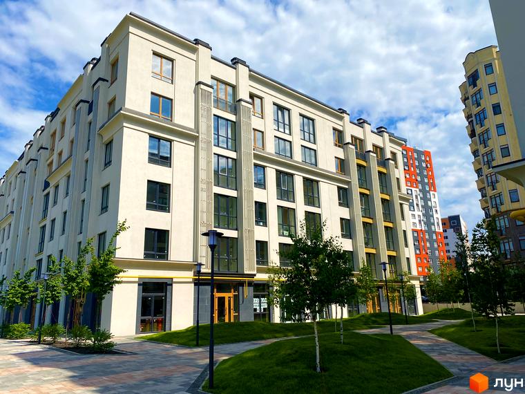 Зображення фасаду та прибудинкової території Житлового комплексу Бургундія. Навколо будинку зелені насадження та тротуарна плитка.